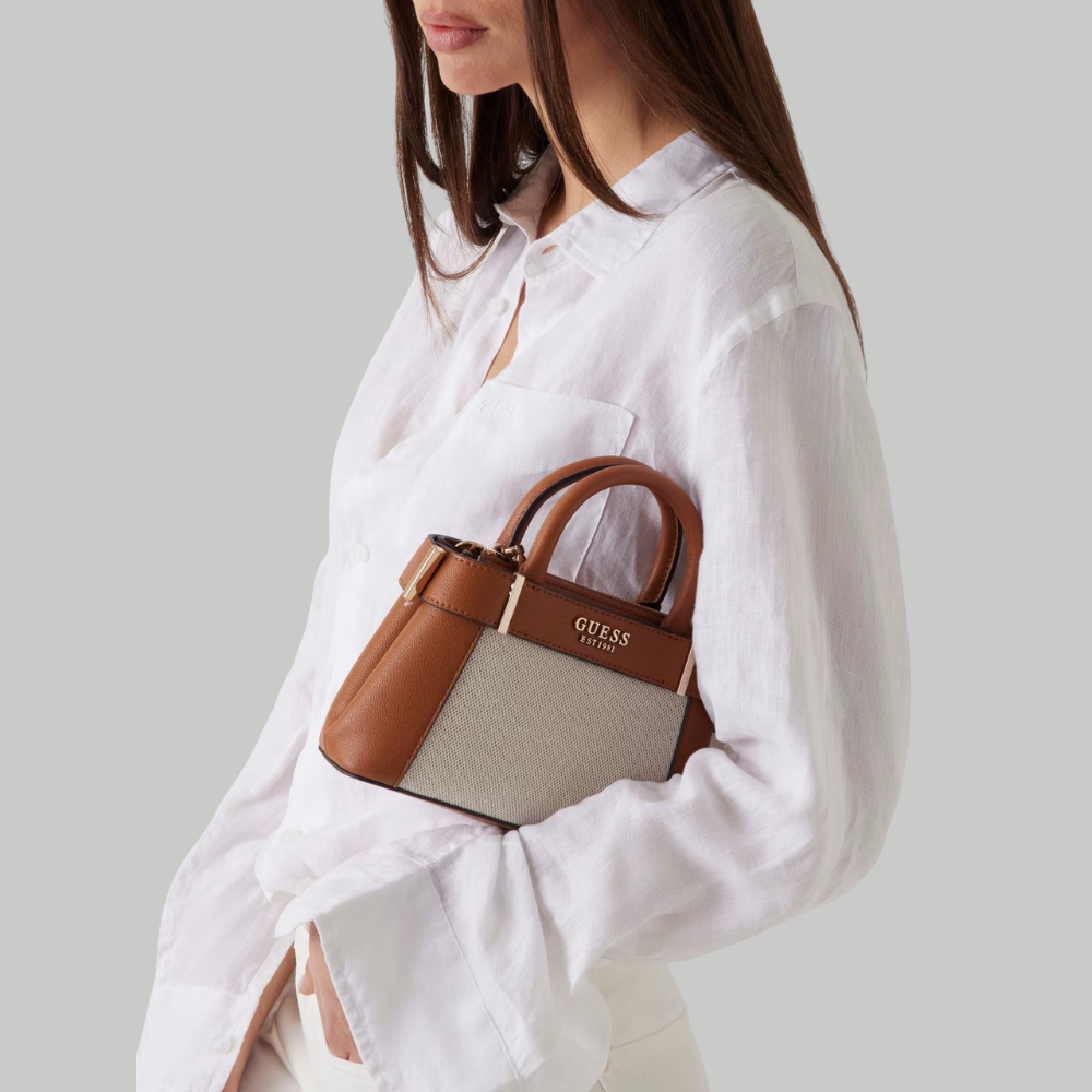 Woman holding a Guess handbag against a plain background